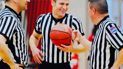 Basketball officials in Honig's striped uniforms sharing a laugh courtside